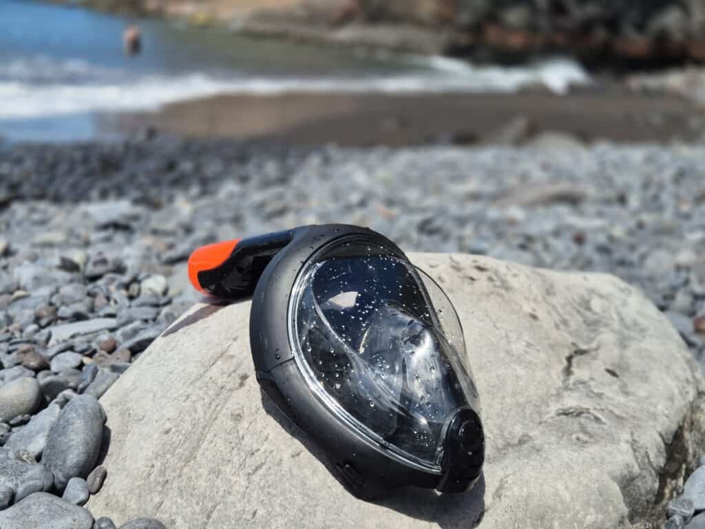 Snorkelmasker met waterdruppels ligt op een rots aan een kiezelstrand op Madeira, met de zee op de achtergrond – klaar voor een duik in het heldere water van Madeira. Snorkelen op Madeira.